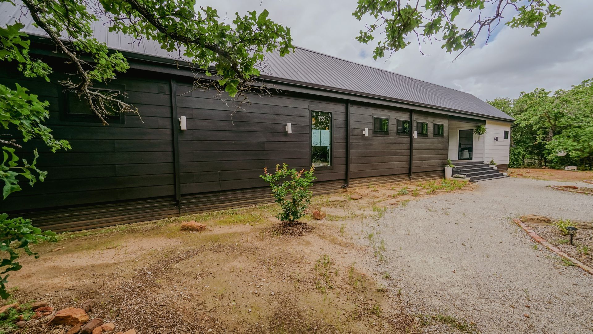 Black wooden building with a dark roof and a gravel driveway.