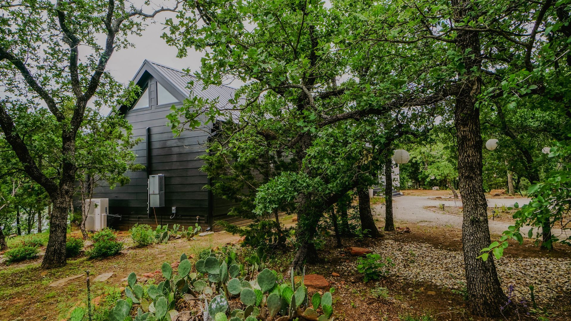 Modern gray house nestled in a green, wooded area.