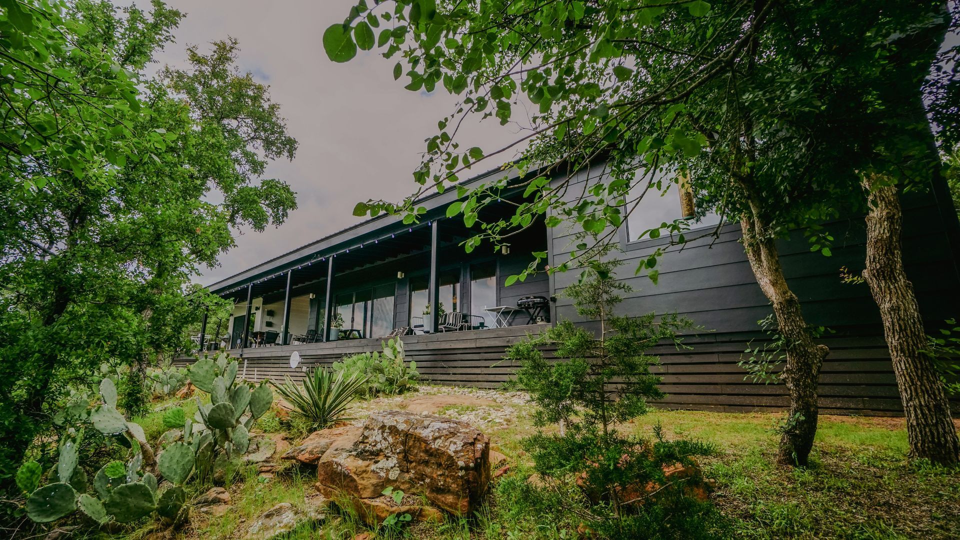 Modern house with a long porch, viewed through trees and cacti.