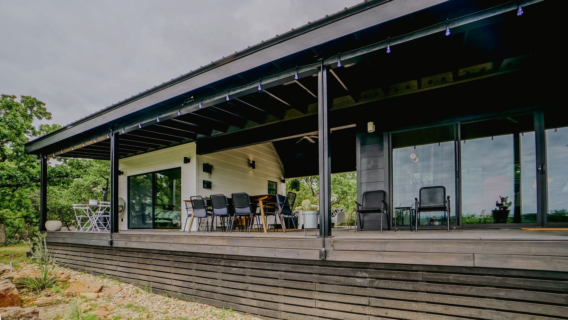 A modern, single-story house with a long veranda, black roof, and large windows.