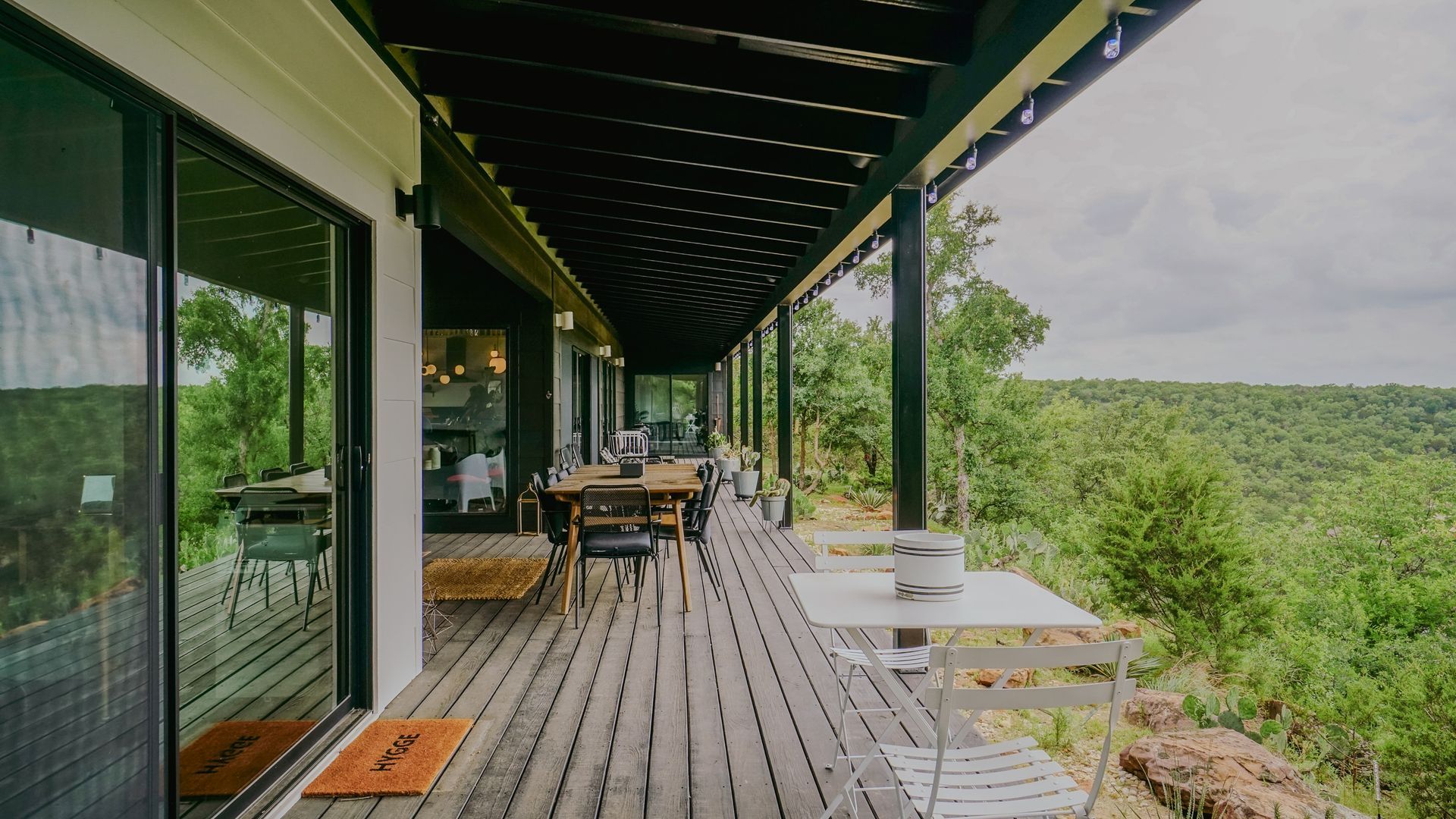 Wooden deck with outdoor dining overlooking a lush, green landscape, beneath a shaded overhang.