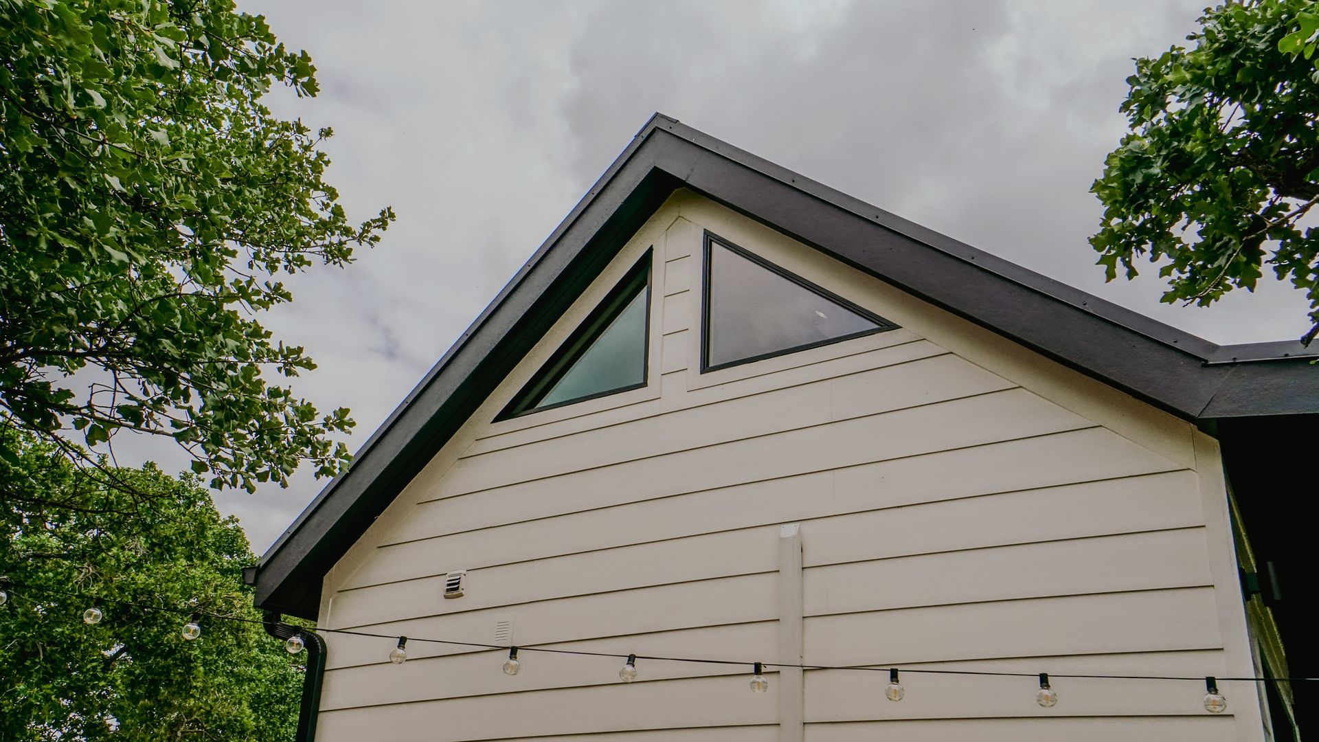 White house exterior with dark roof and triangular windows, visible against a cloudy sky.