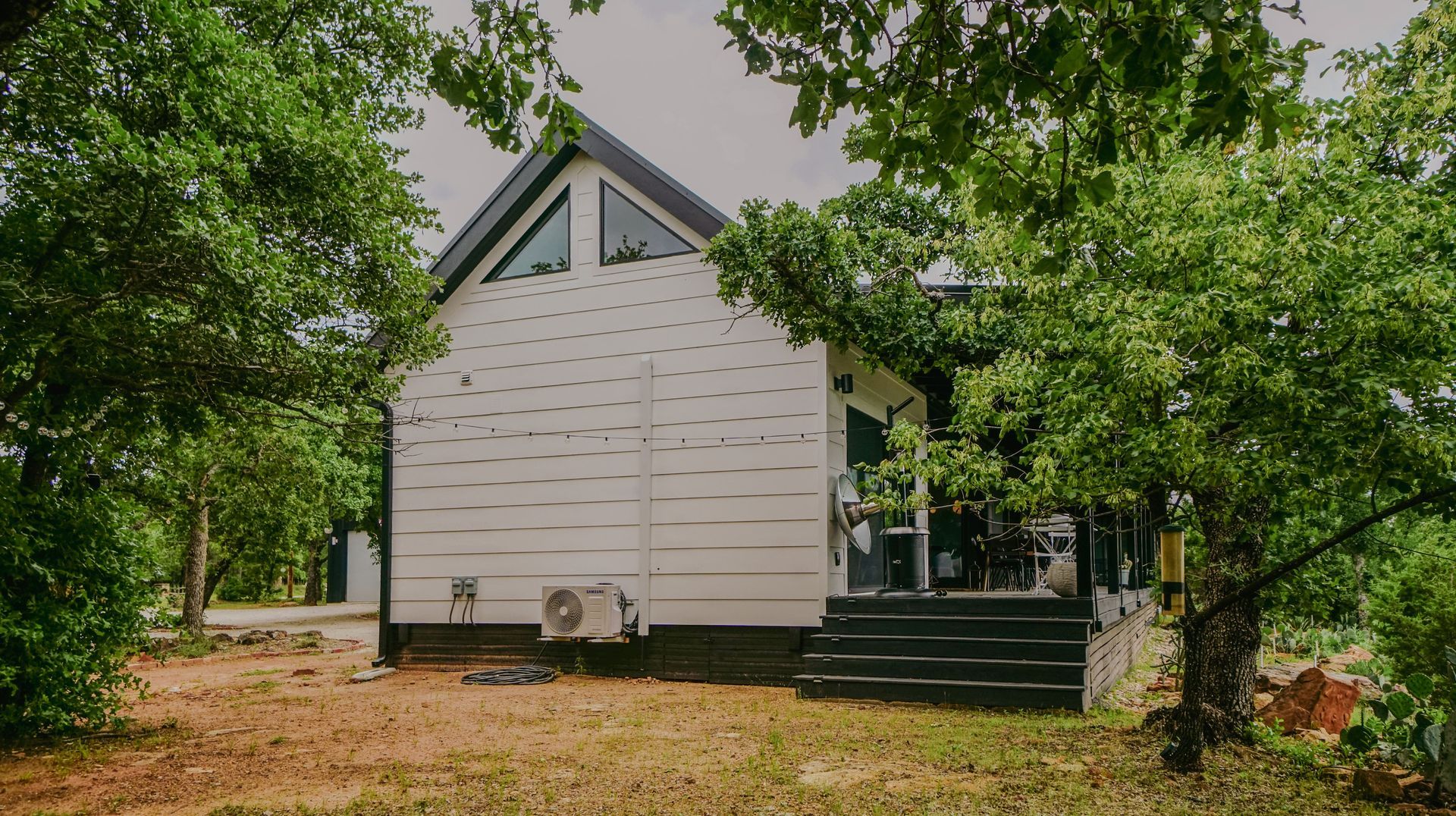 White cabin with black trim, surrounded by trees, with small porch.