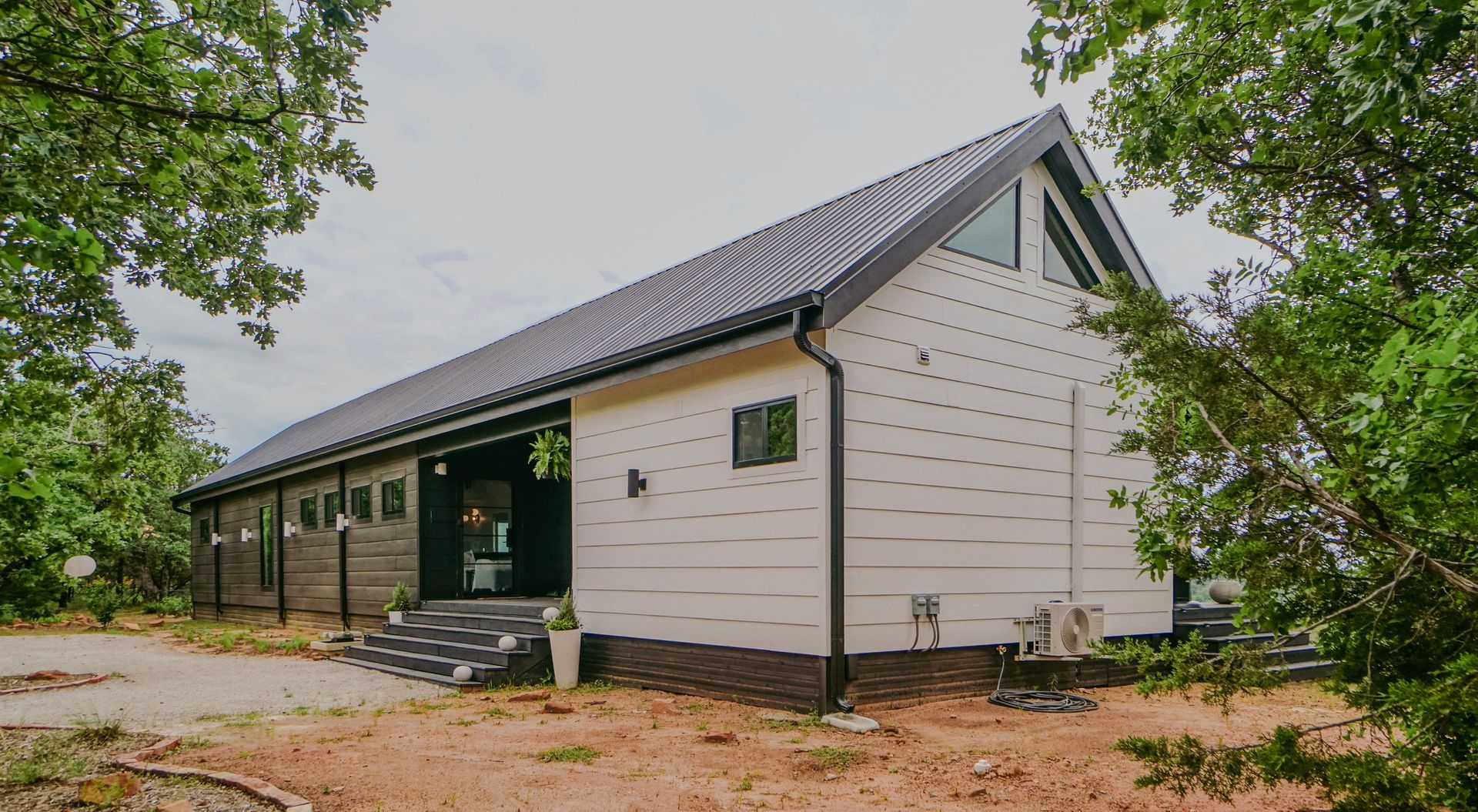 Modern white building with black roof, nestled among trees, on a cloudy day.