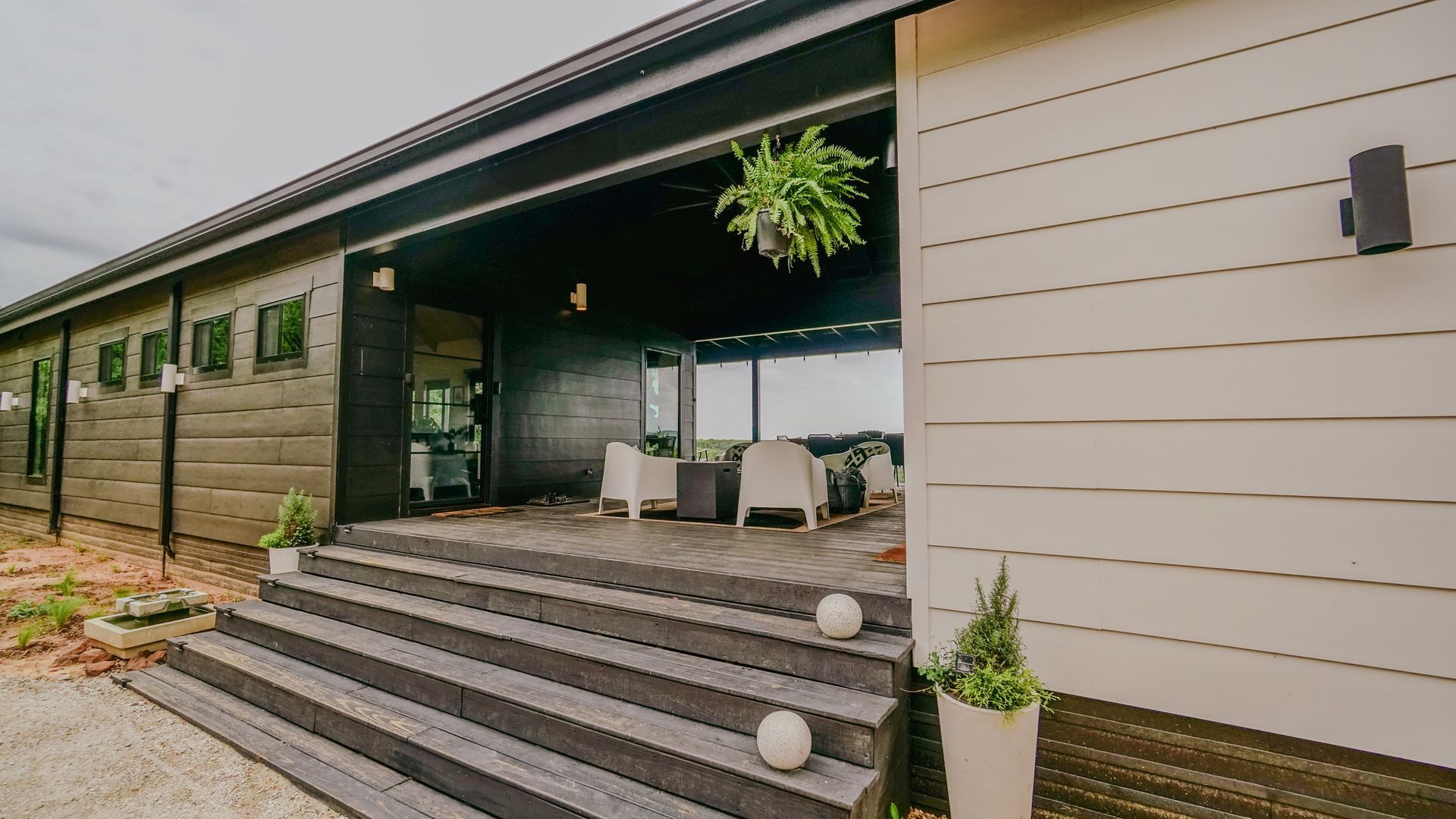 Modern home exterior with covered porch and steps. Grey and white siding, potted plants.