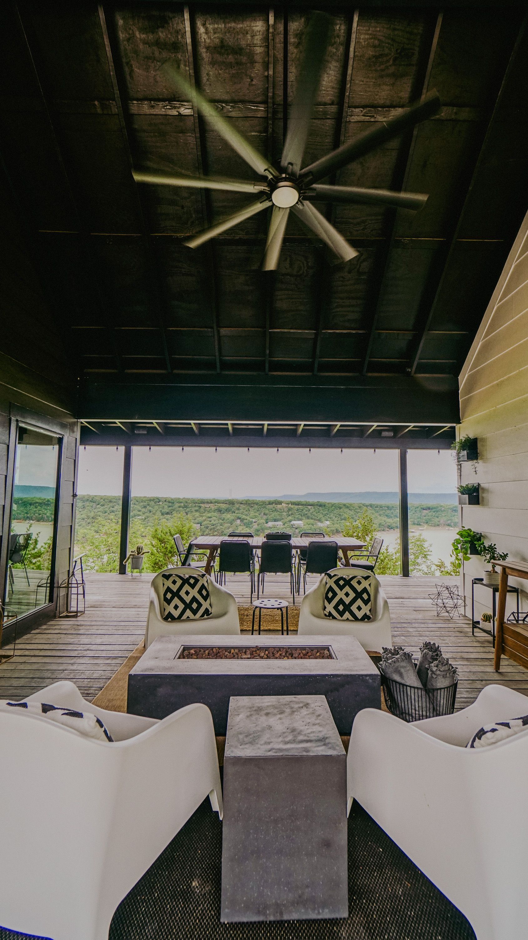 Outdoor covered patio with modern furniture, lake view, and large ceiling fan.