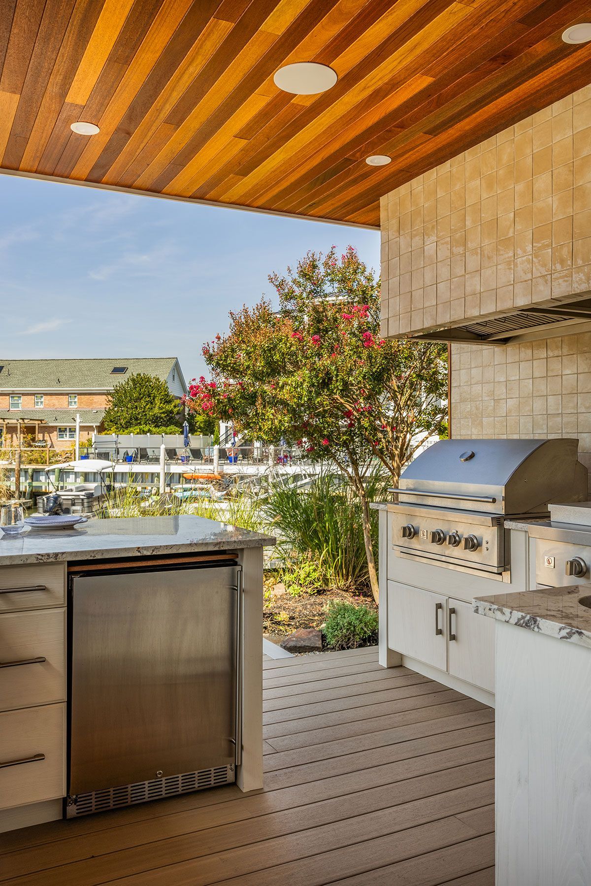 Outdoor patio with built-in grill, stainless cabinet, wood ceiling, and landscaped view beyond open railing