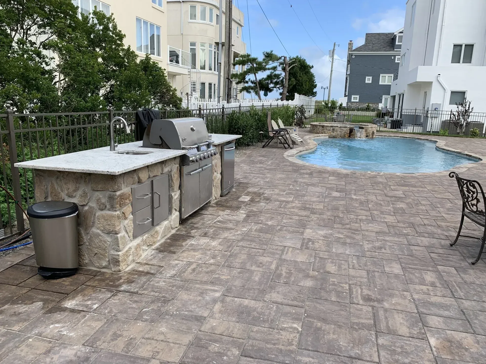 Poolside patio with stone grill, trash can, and curved swimming pool beside apartment buildings
