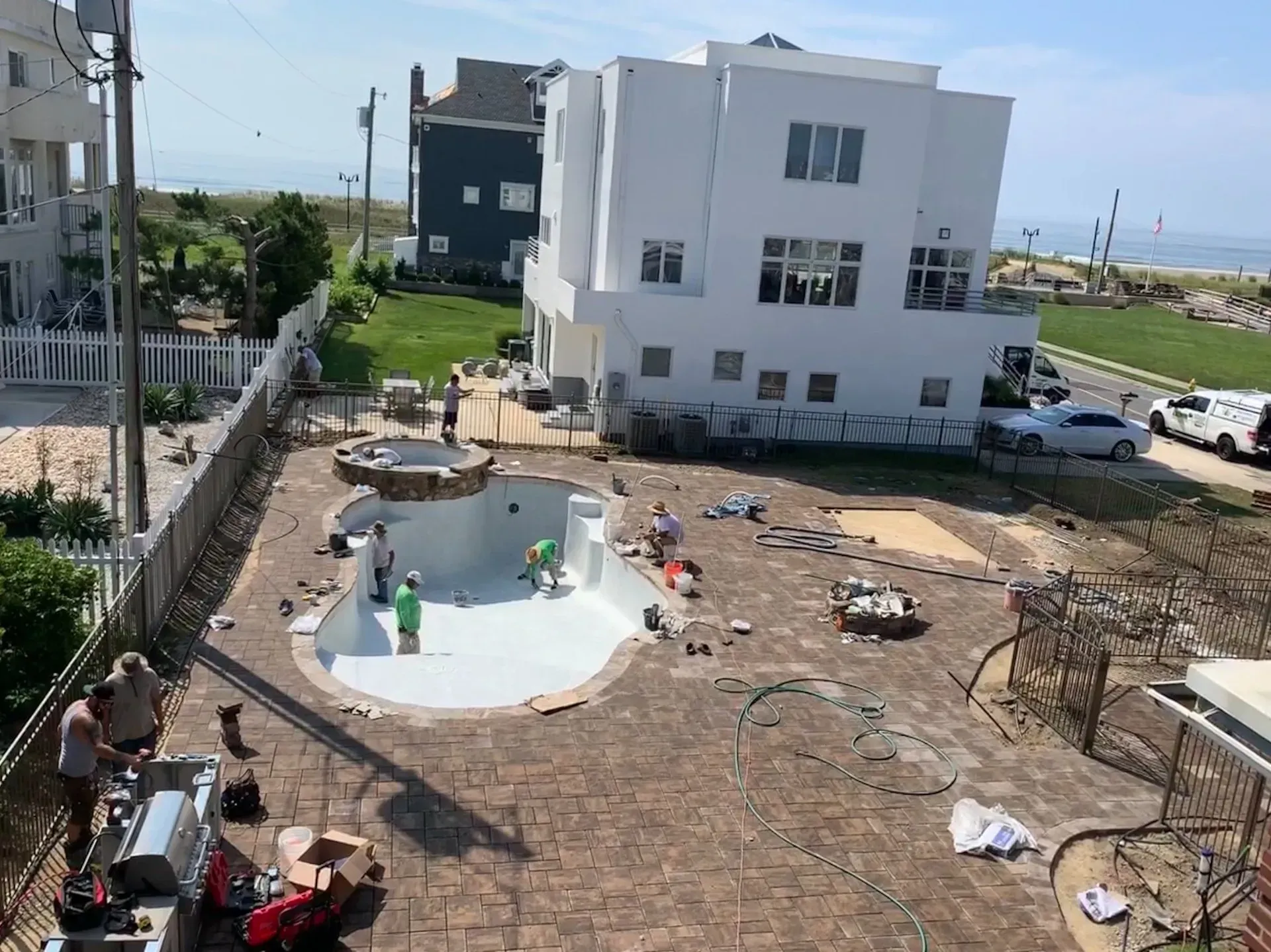 Courtyard with a small empty white pool, scattered people, and a white apartment building by the sea