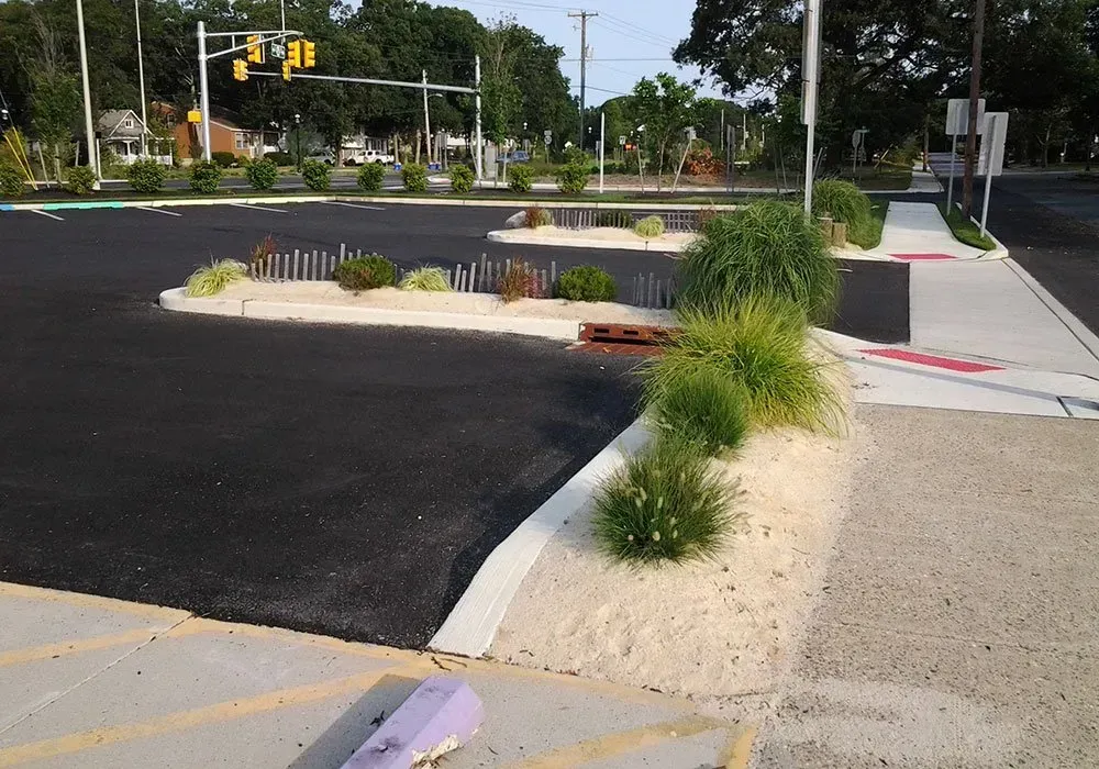 Raised curb and landscaped median beside an asphalt street at a traffic intersection, with traffic lights in the distance