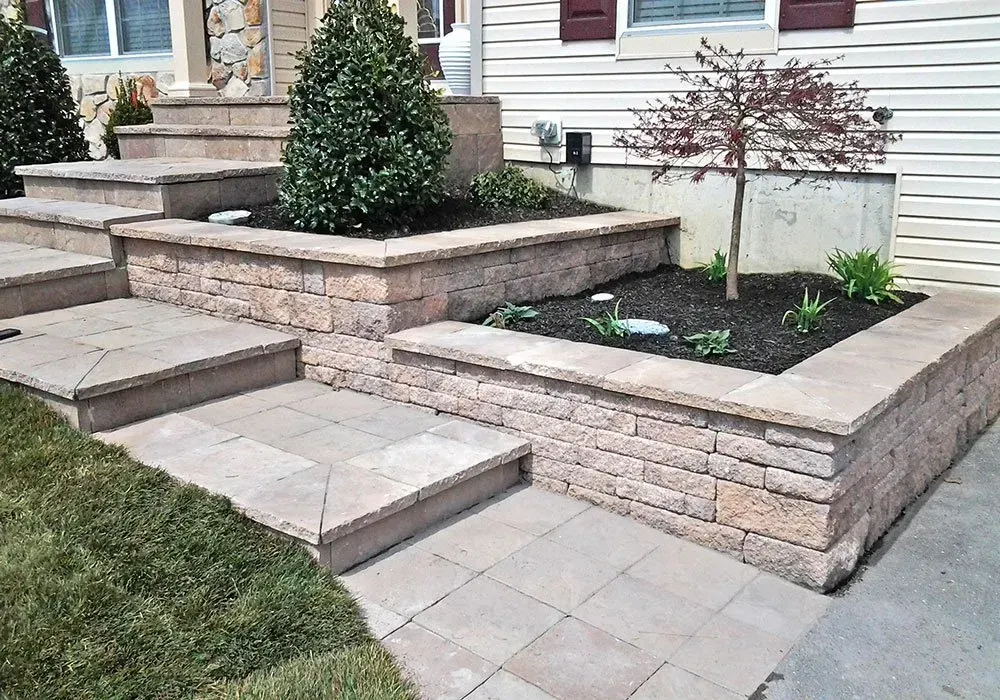 Stone raised garden beds with shrubs beside a house entrance