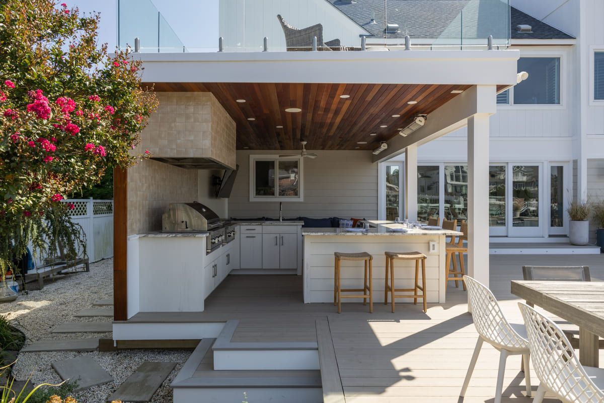 Modern outdoor kitchen and patio with bar seating, white cabinetry, wood سقف, and lounge chairs