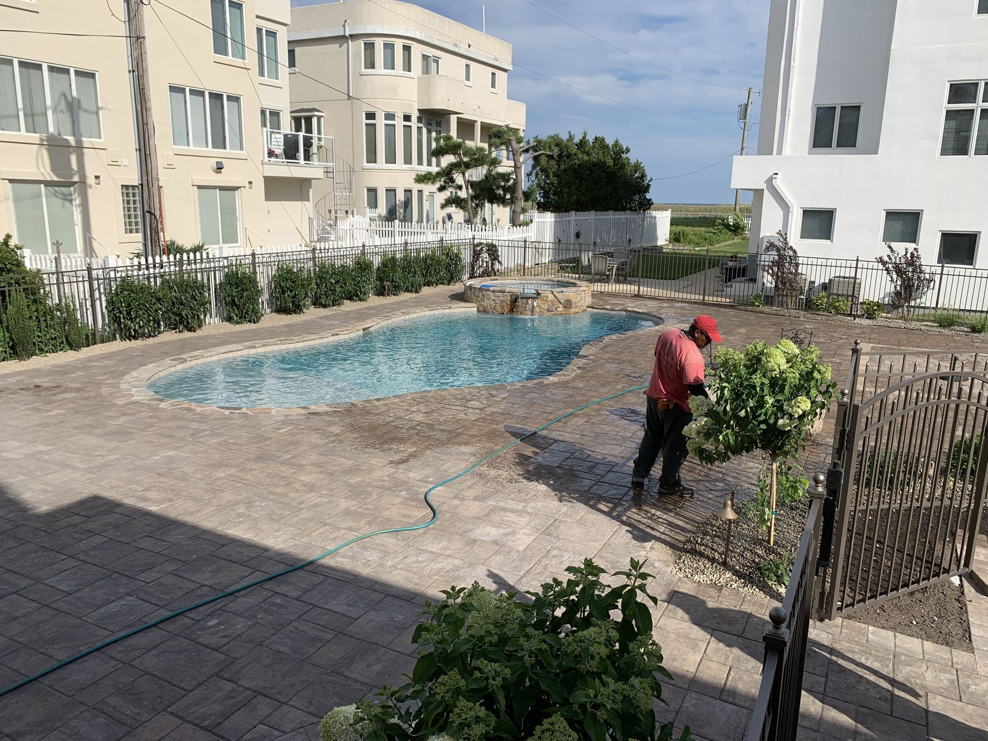 Courtyard pool with a person in a red shirt watering plants beside apartment buildings