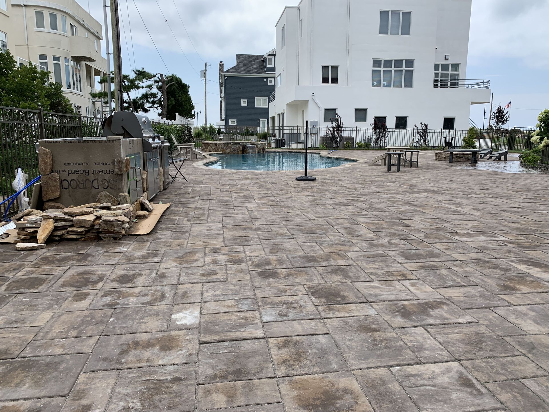 Empty stone courtyard beside a pool, with white buildings under an overcast sky.