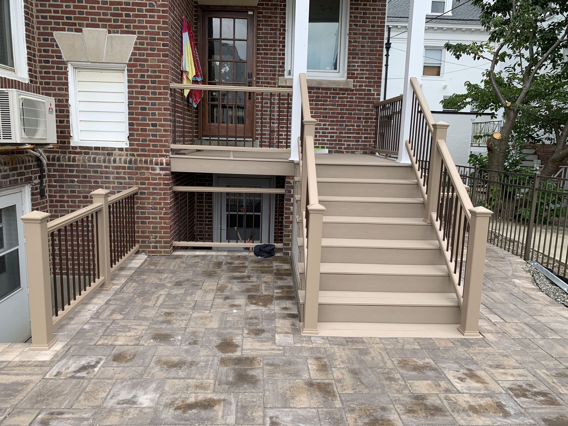 Brick house entrance with front steps, ramp, and stone patio leading to a basement door