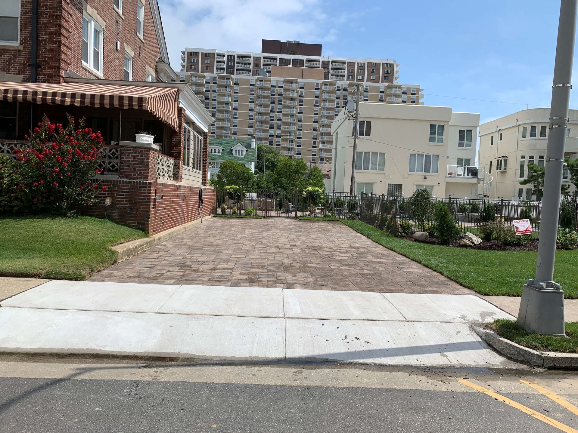 Brick building entrance with cobblestone path, sidewalk curb ramp, and apartment buildings in the background