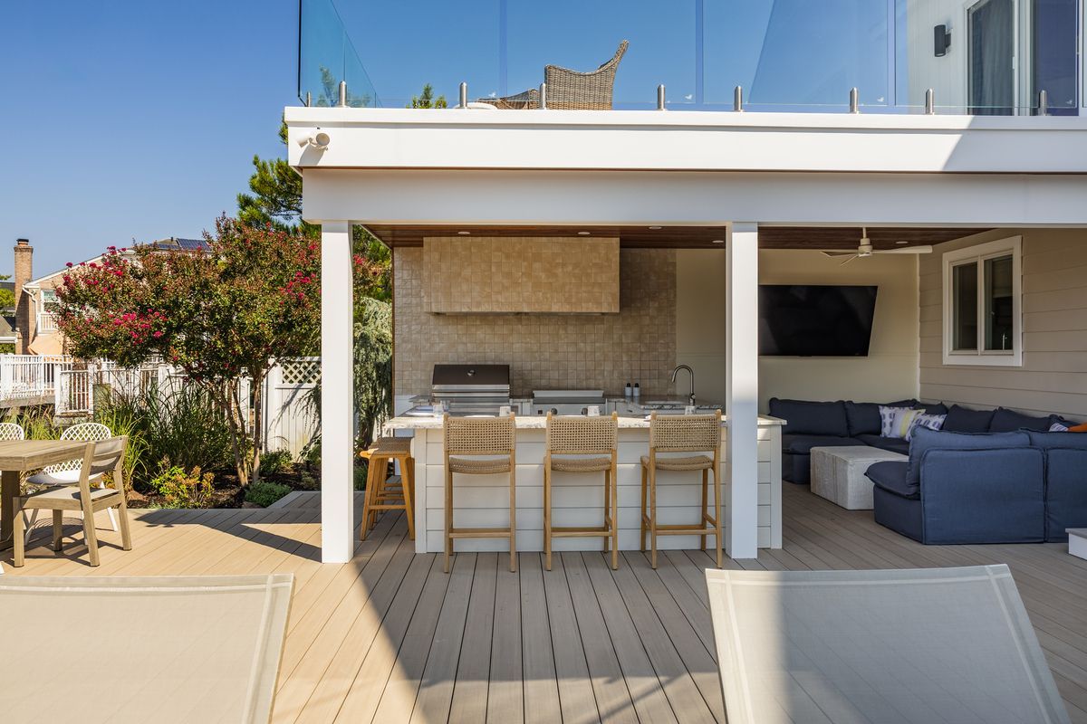 Outdoor patio with a white pergola, wicker dining set, and blue lounge seating by a modern house