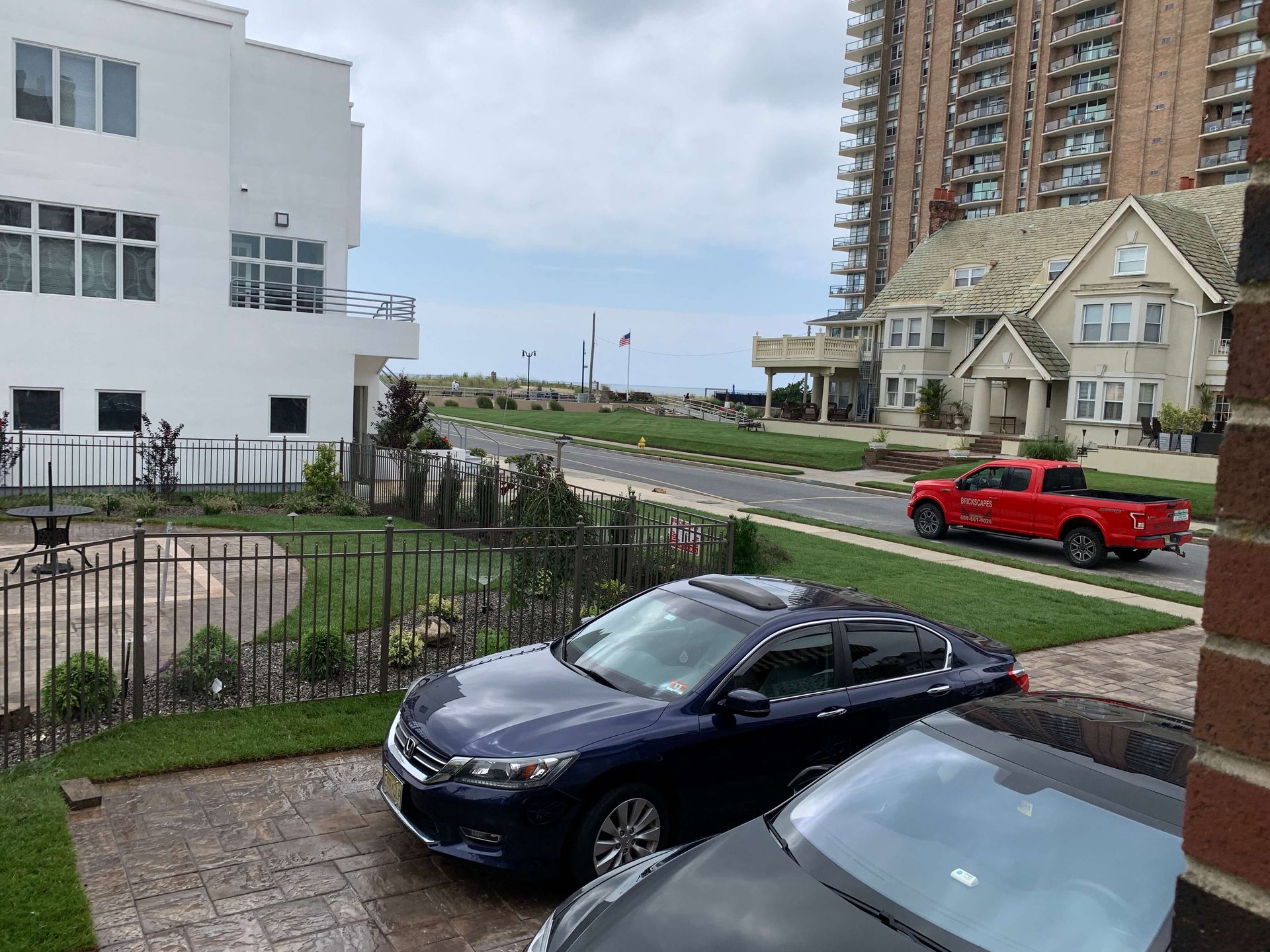 Street view with parked cars, a white building, and a red pickup near a waterfront walkway