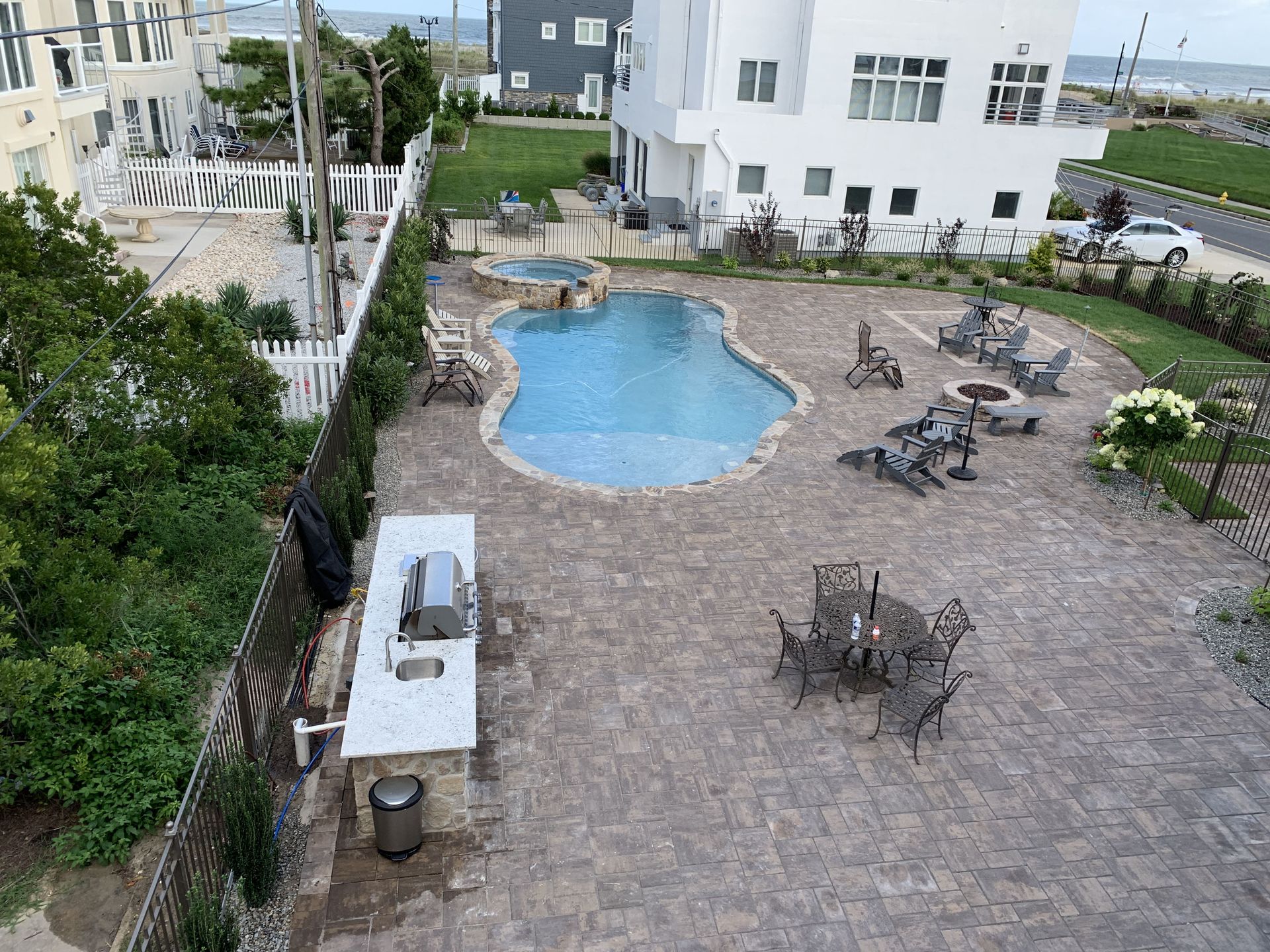 Courtyard with a small blue pool, stone patio, tables, chairs, and surrounding greenery and buildings