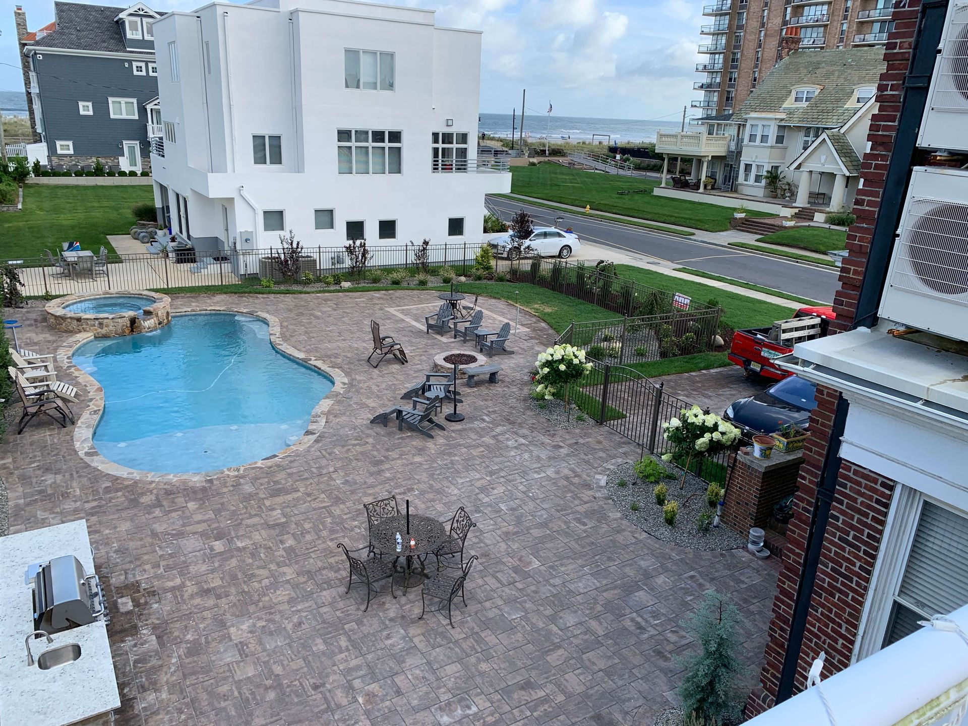 Courtyard with a small blue pool, patio tables, and white apartment buildings beside a street.