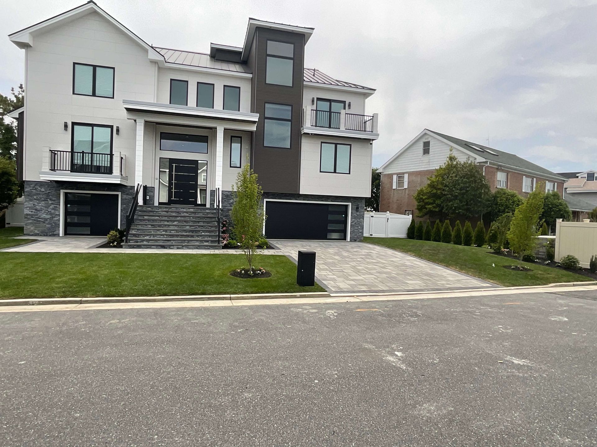 Modern white-and-gray multi-story townhouse with stairs, garage, and front lawn on a quiet street