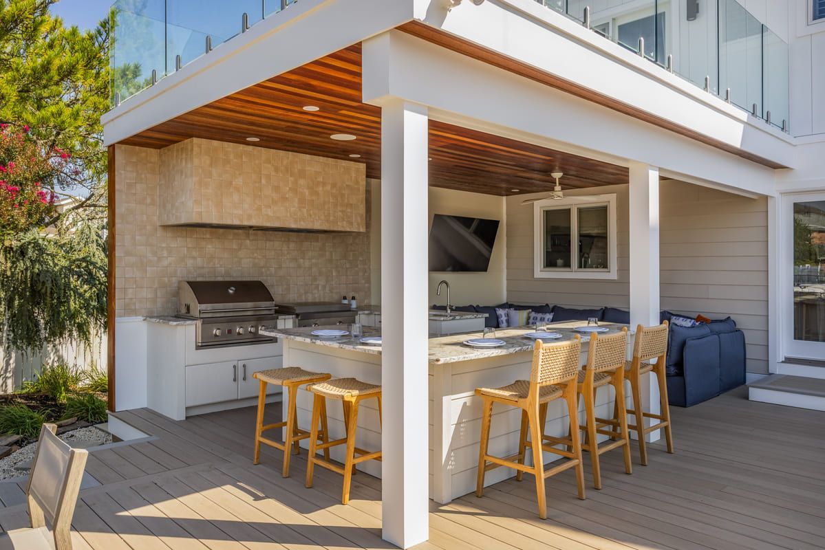 Outdoor patio with built-in grill, sink, bar stools, and dining area under a wooden pergola