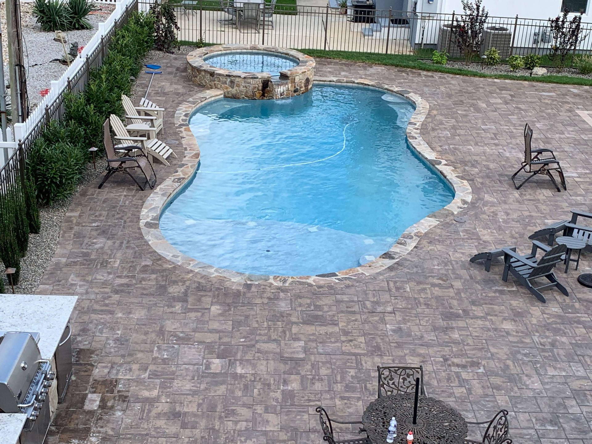 Backyard swimming pool with stone patio, lounge chairs, and a small spa area