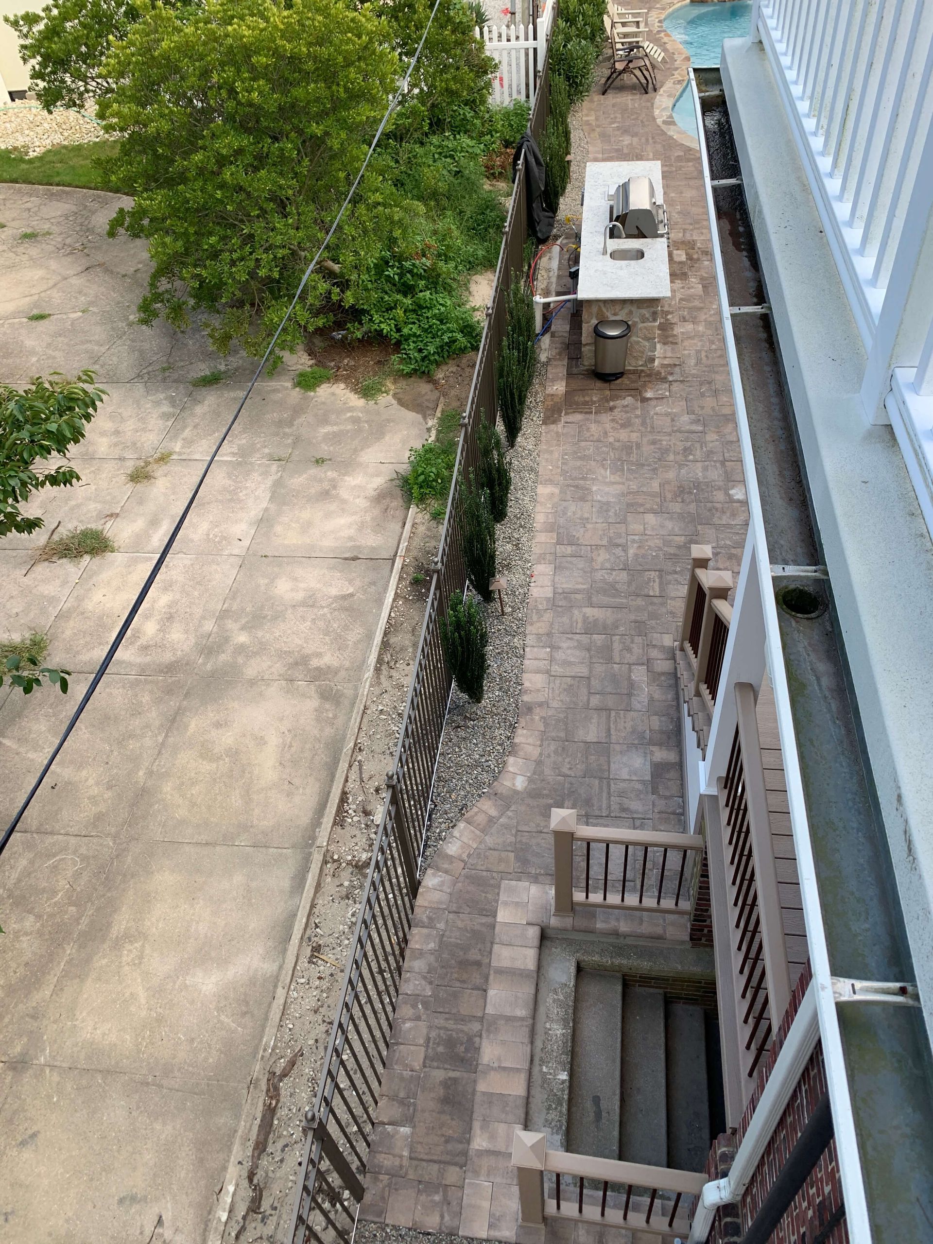 Aerial view of a narrow alley beside a building, with trees, concrete paths, and utility units.