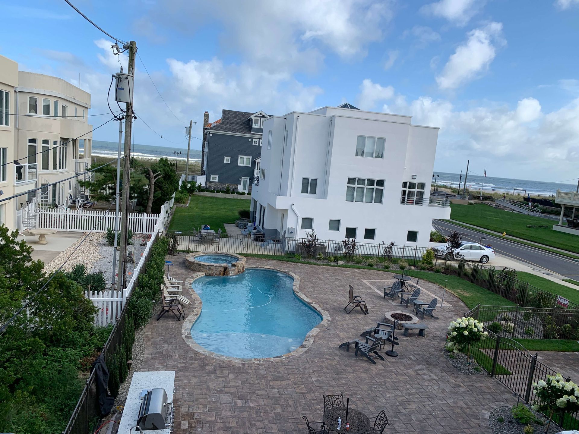 Courtyard with a swimming pool, lounge chairs, and white apartment buildings under a partly cloudy sky