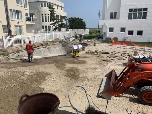 Construction site with excavators and workers in a dirt lot between apartment buildings