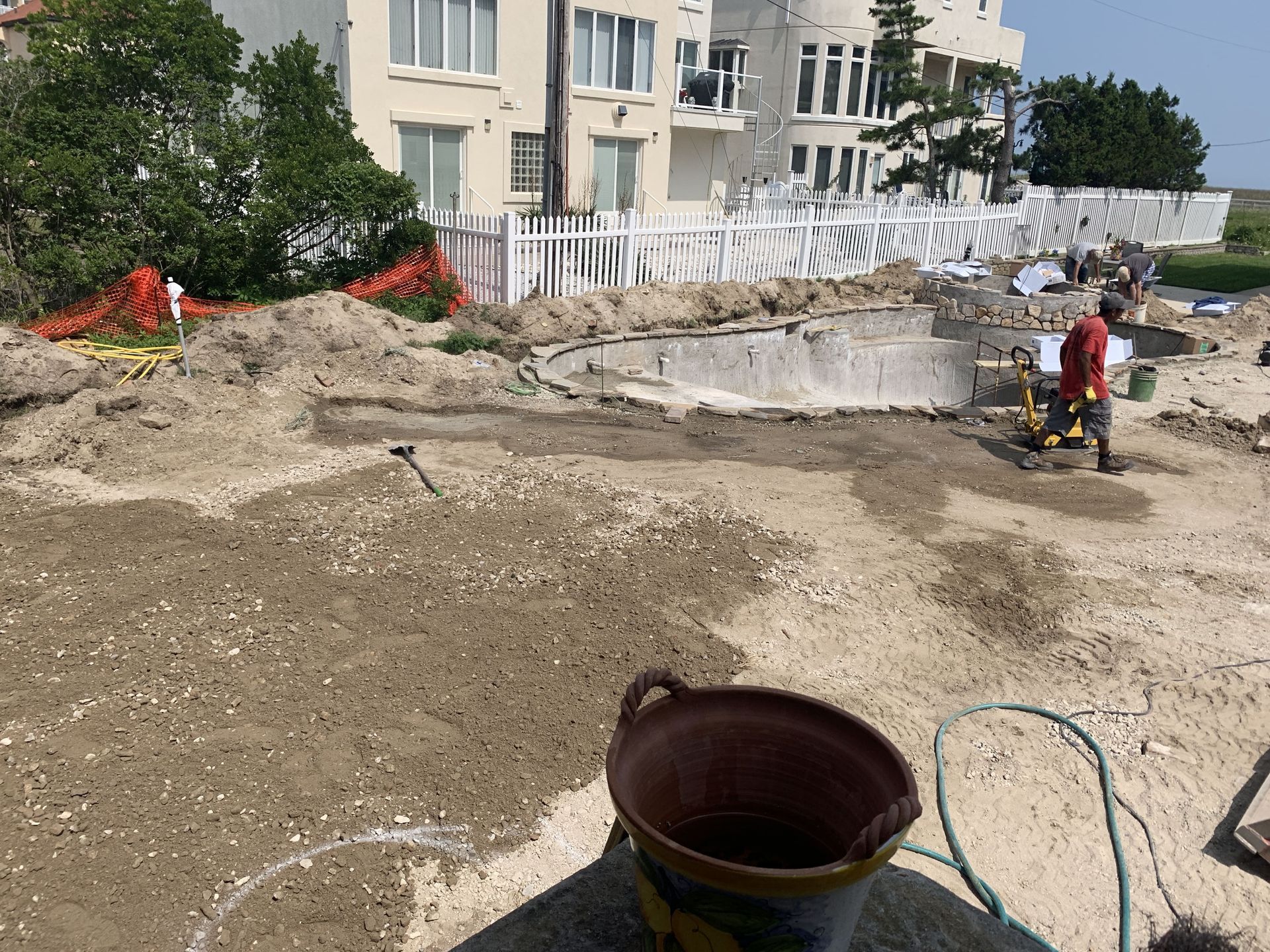 Construction site with excavated dirt, a worker by a yellow machine, and apartment buildings in the background