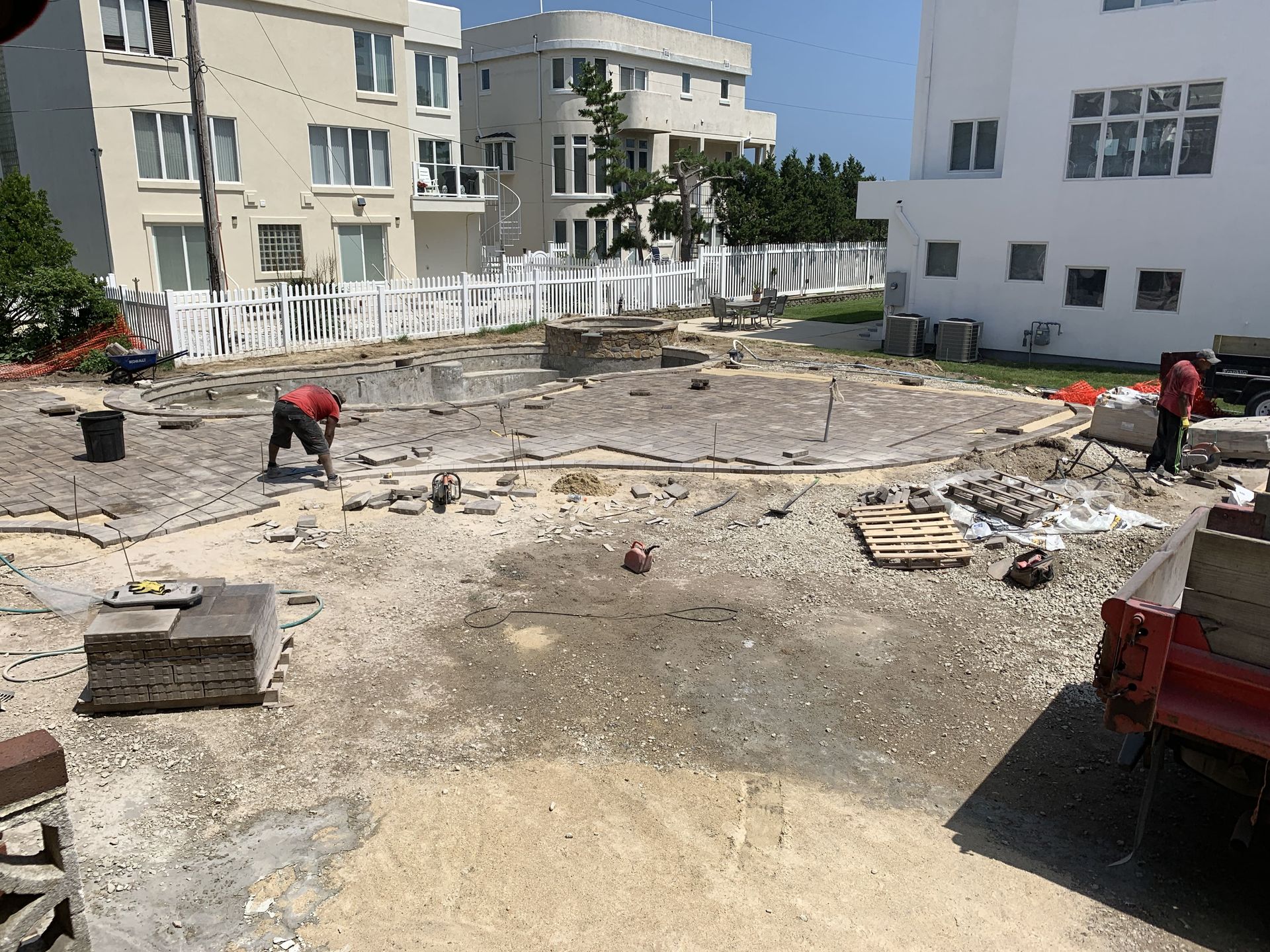 Construction site with workers leveling a dirt lot beside apartment buildings