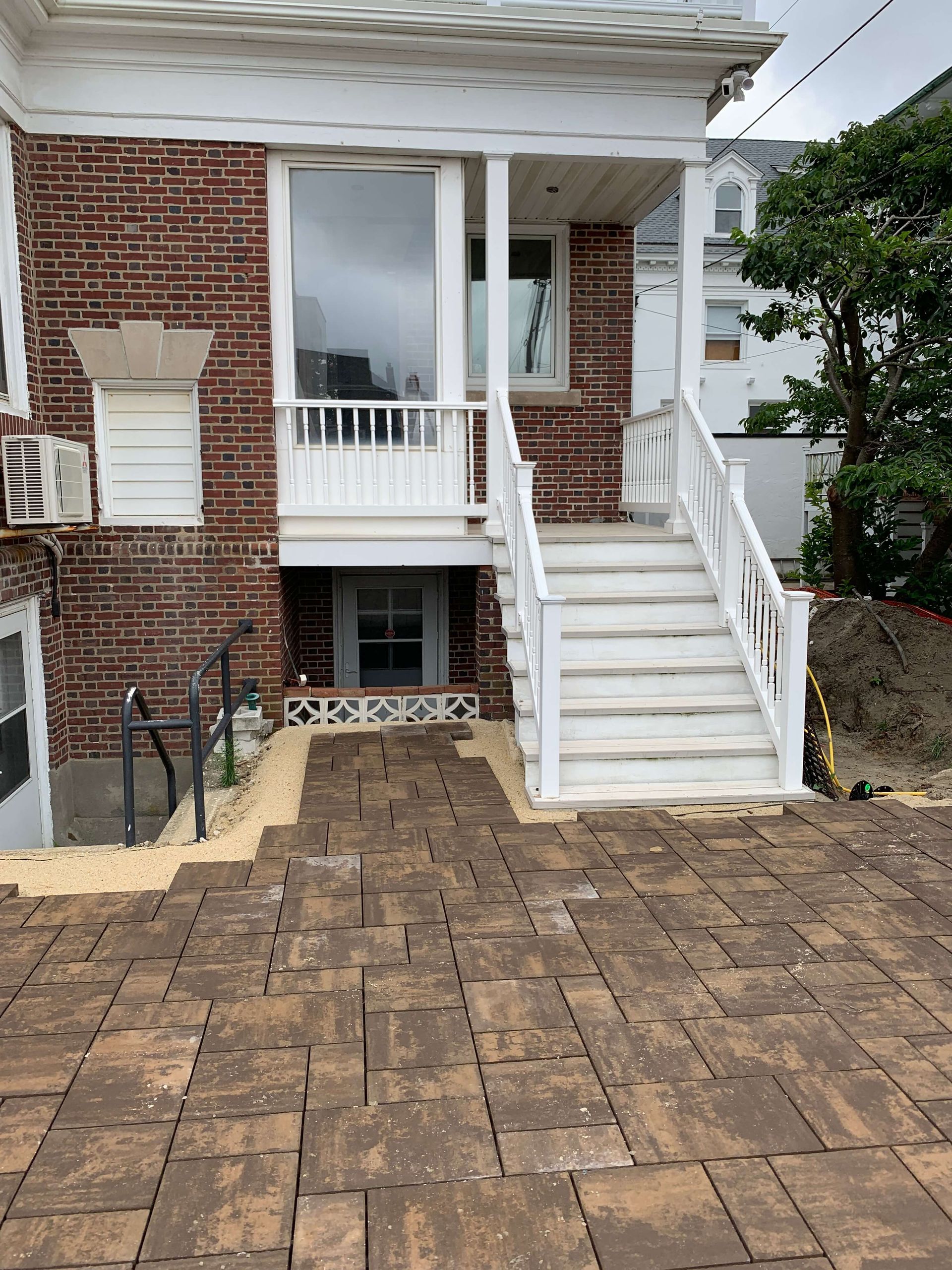 Brick house front with white porch, stairs, and paved driveway leading to the entrance