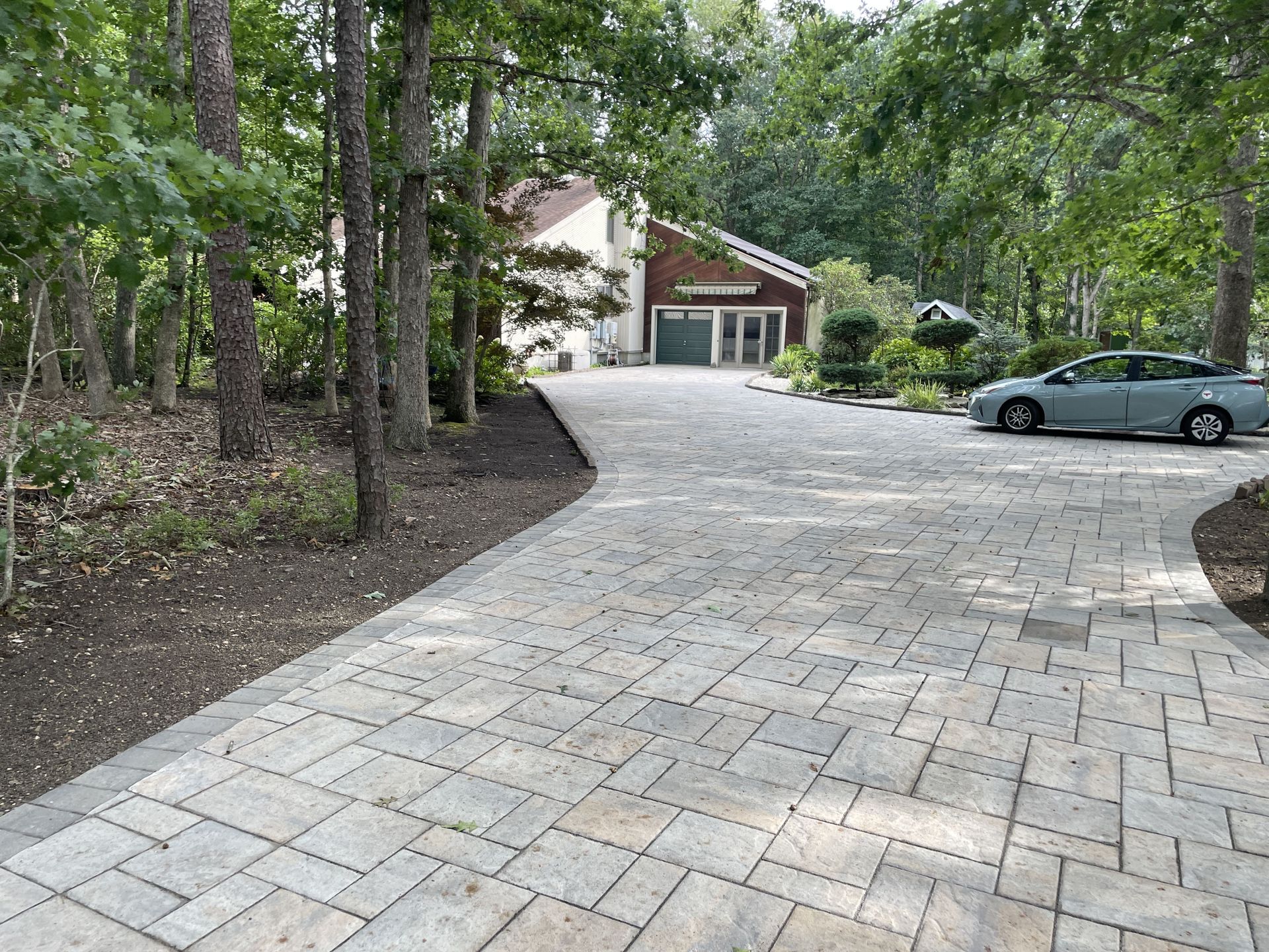 Tree-lined driveway leading to a house with a parked silver car on the right.