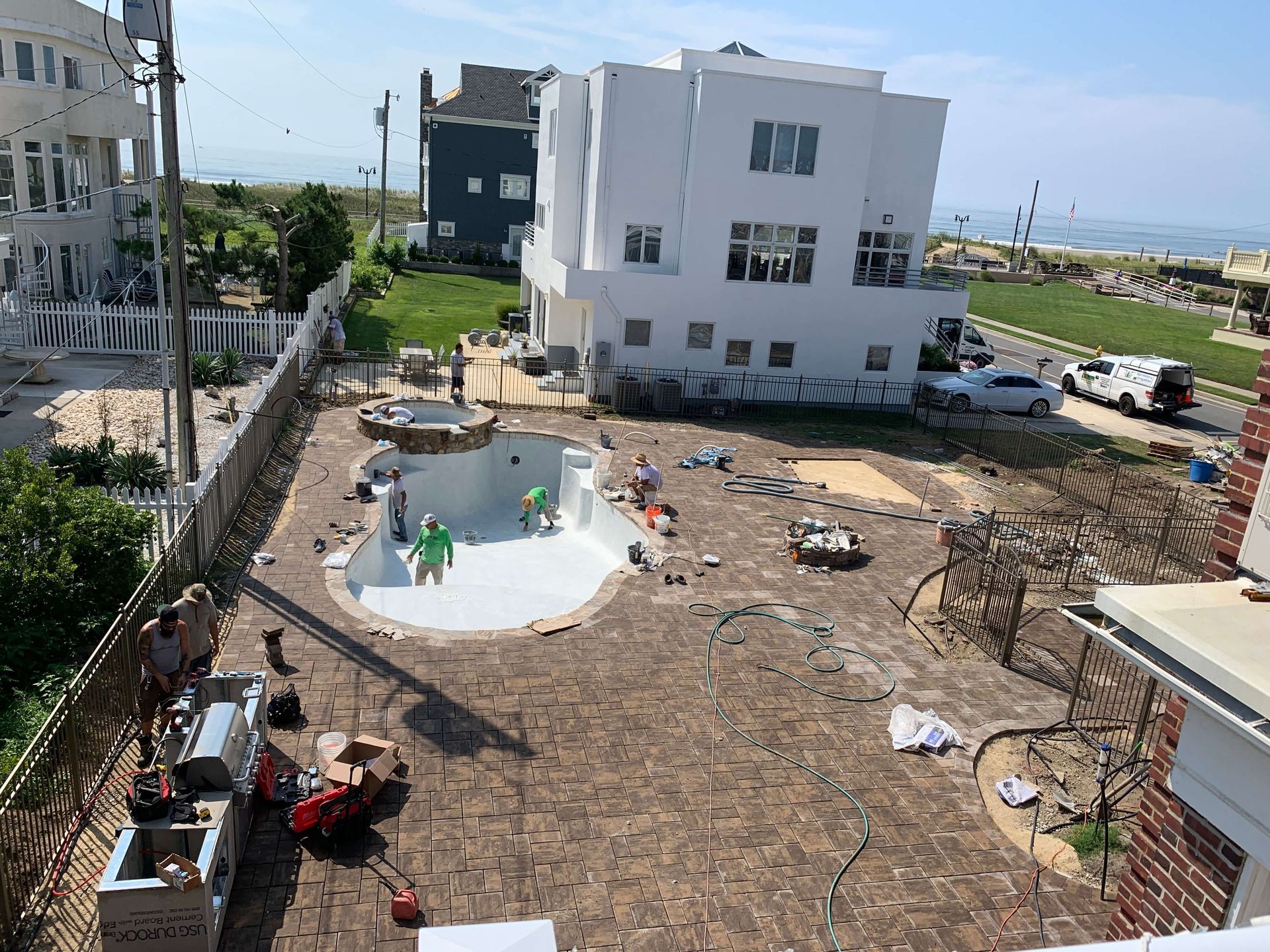 Construction site with white buildings, workers, and a freshly poured concrete area in a residential neighborhood