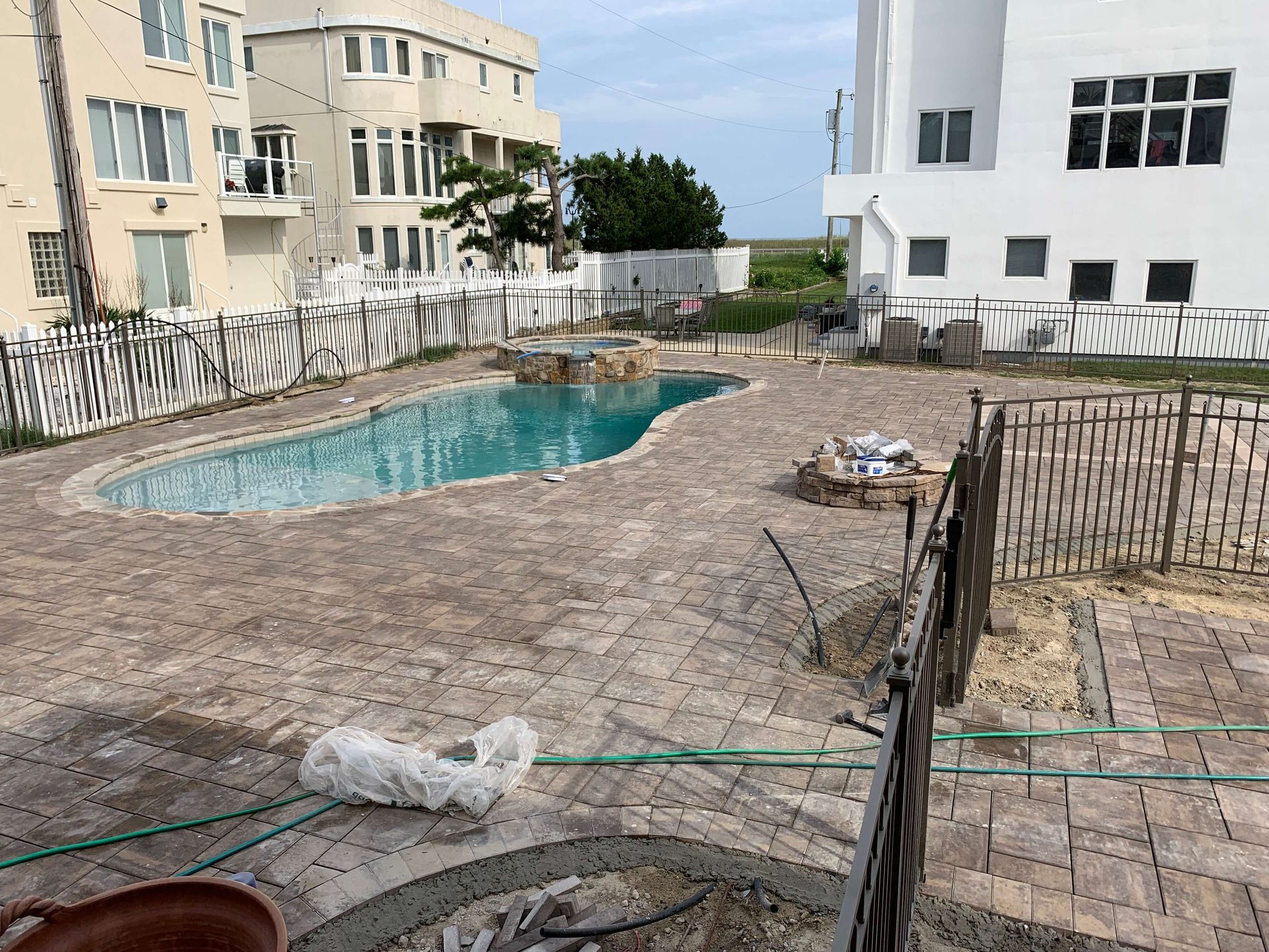 Partially built pool area with rough stone ground, fence, and apartment buildings around it
