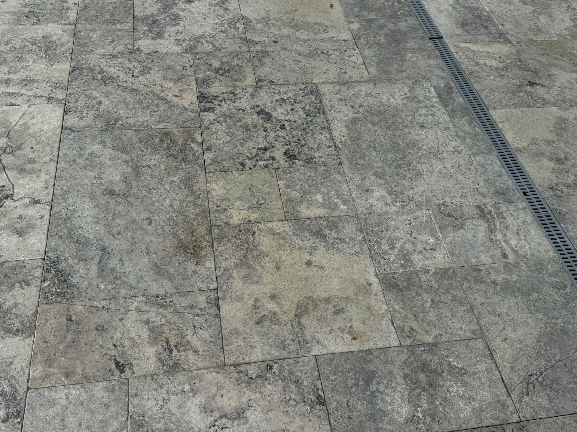 Gray stone pavement with a dark metal drainage grate along the right side.
