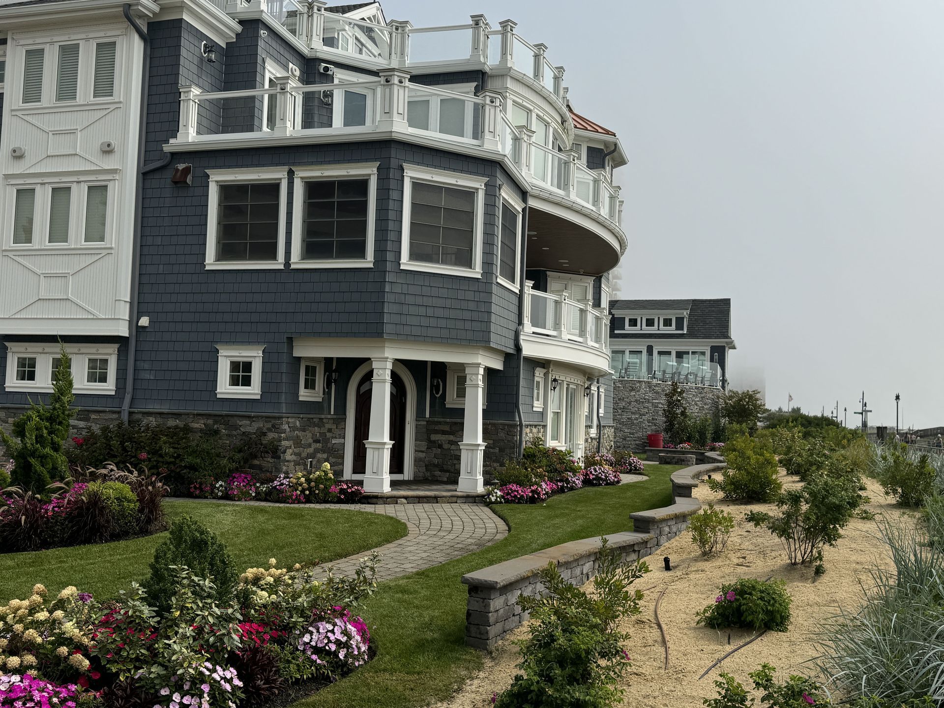 Gray seaside house with white trim, flower garden, and sandy path along the coast