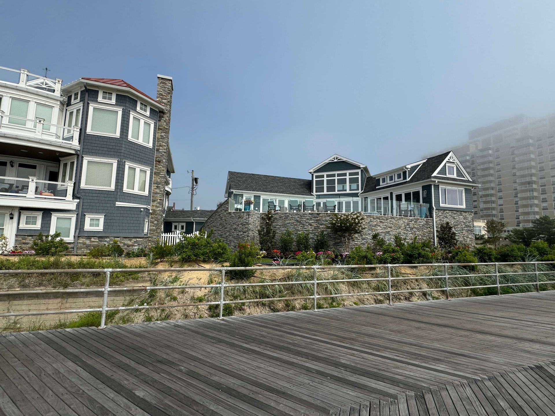 Foggy coastal boardwalk with row of blue and white houses and a railing in front