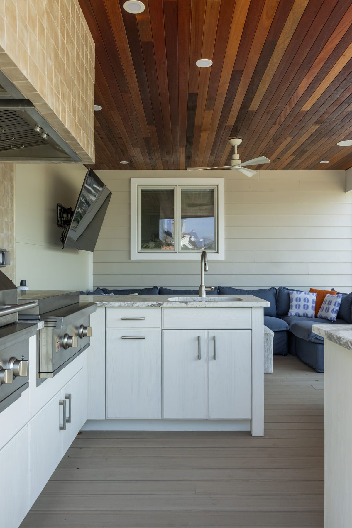 Bright modern outdoor kitchen and lounge with white cabinets, wood ceiling, and gray sectional seating