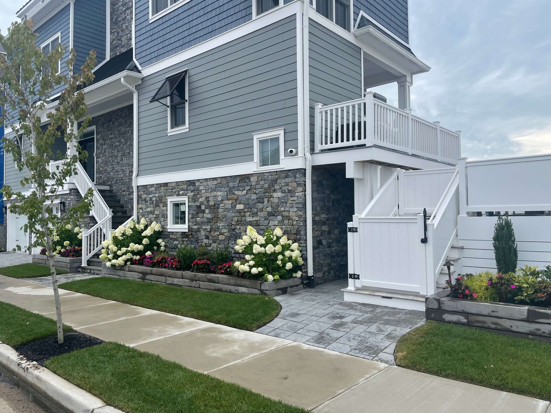 Townhouse exterior with white stairs, gray siding, stone base, and landscaped flower beds along a sidewalk