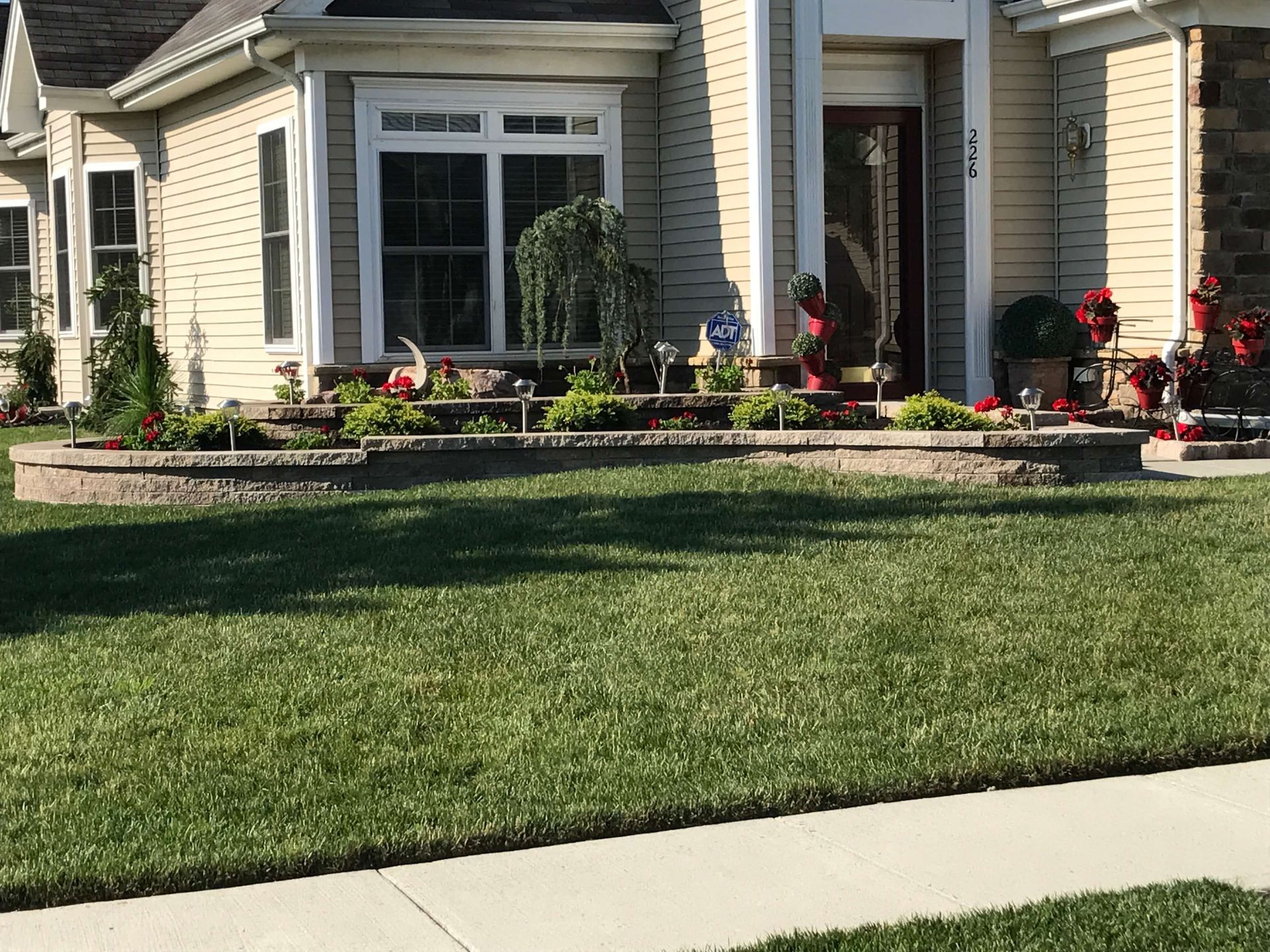 Front yard of a beige house with a large lawn and landscaped flower beds by the porch
