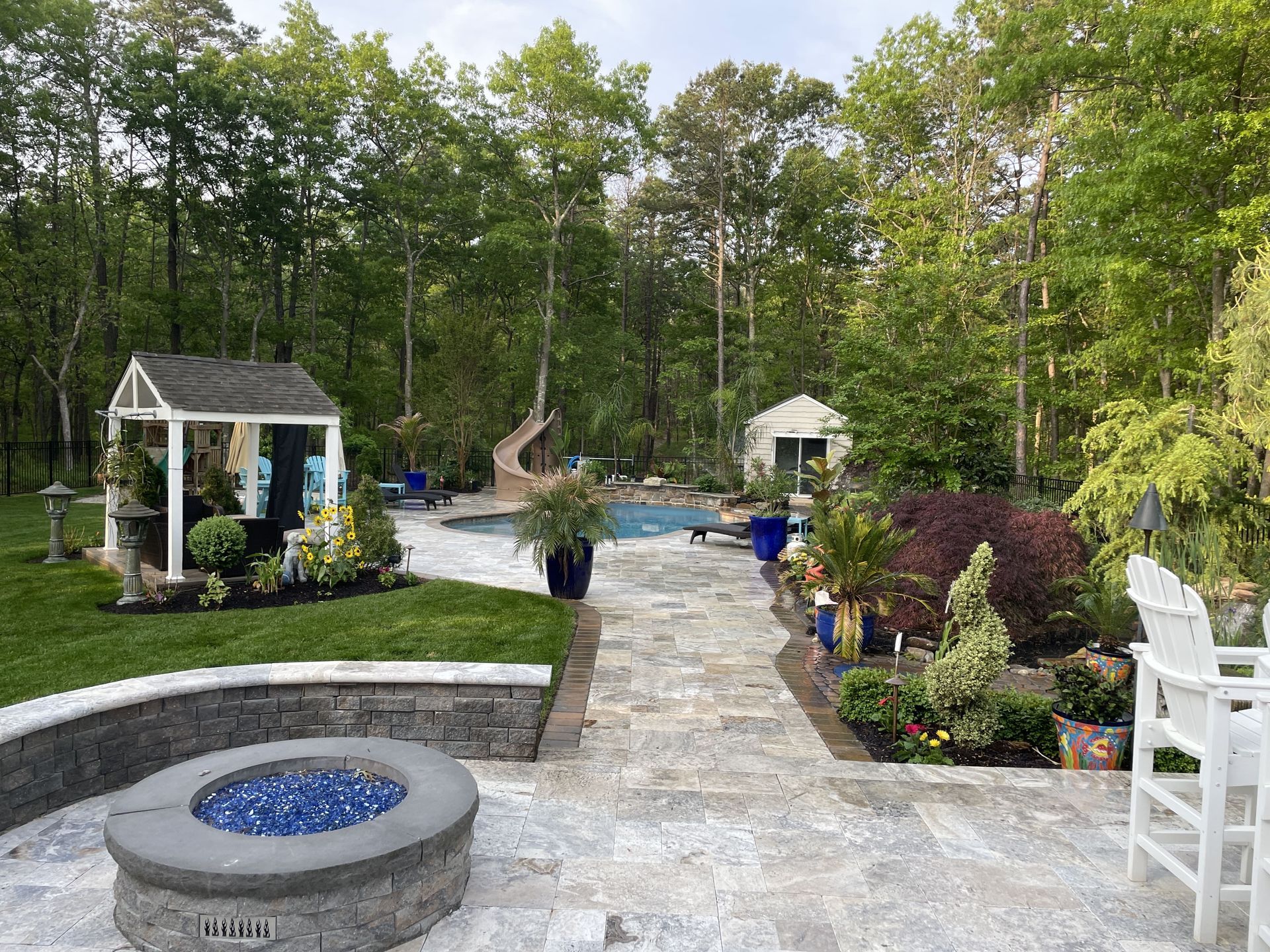 Landscaped backyard patio with stone walkway, fire pit, gazebo, and garden beds