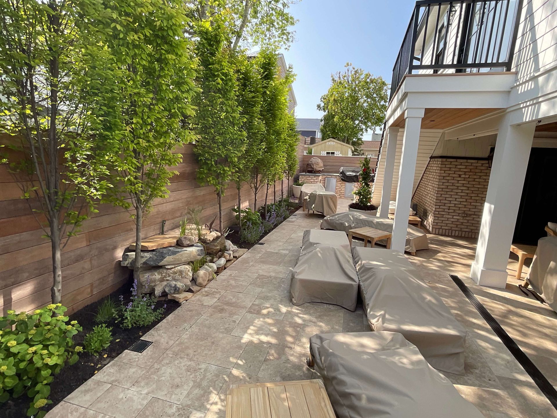 Backyard patio under construction with covered furniture, trees, and a brick privacy wall
