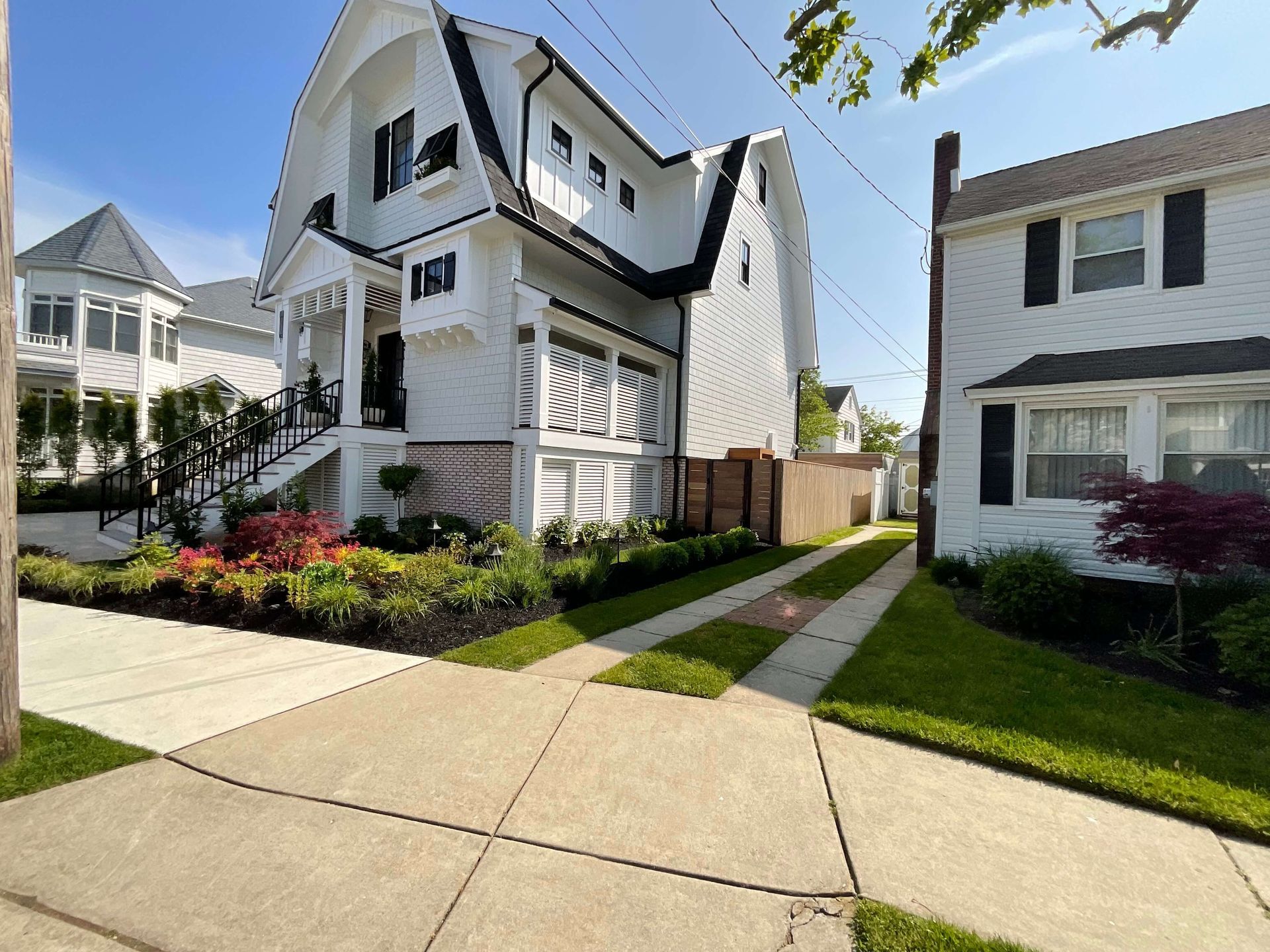Modern white house with curved roof, front walkway, green lawn, and landscaped flower bed on a sunny day
