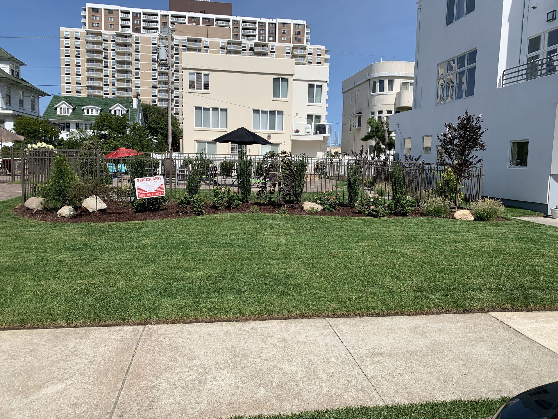 Apartment courtyard with green lawn, sidewalk, flower beds, and modern buildings in the background