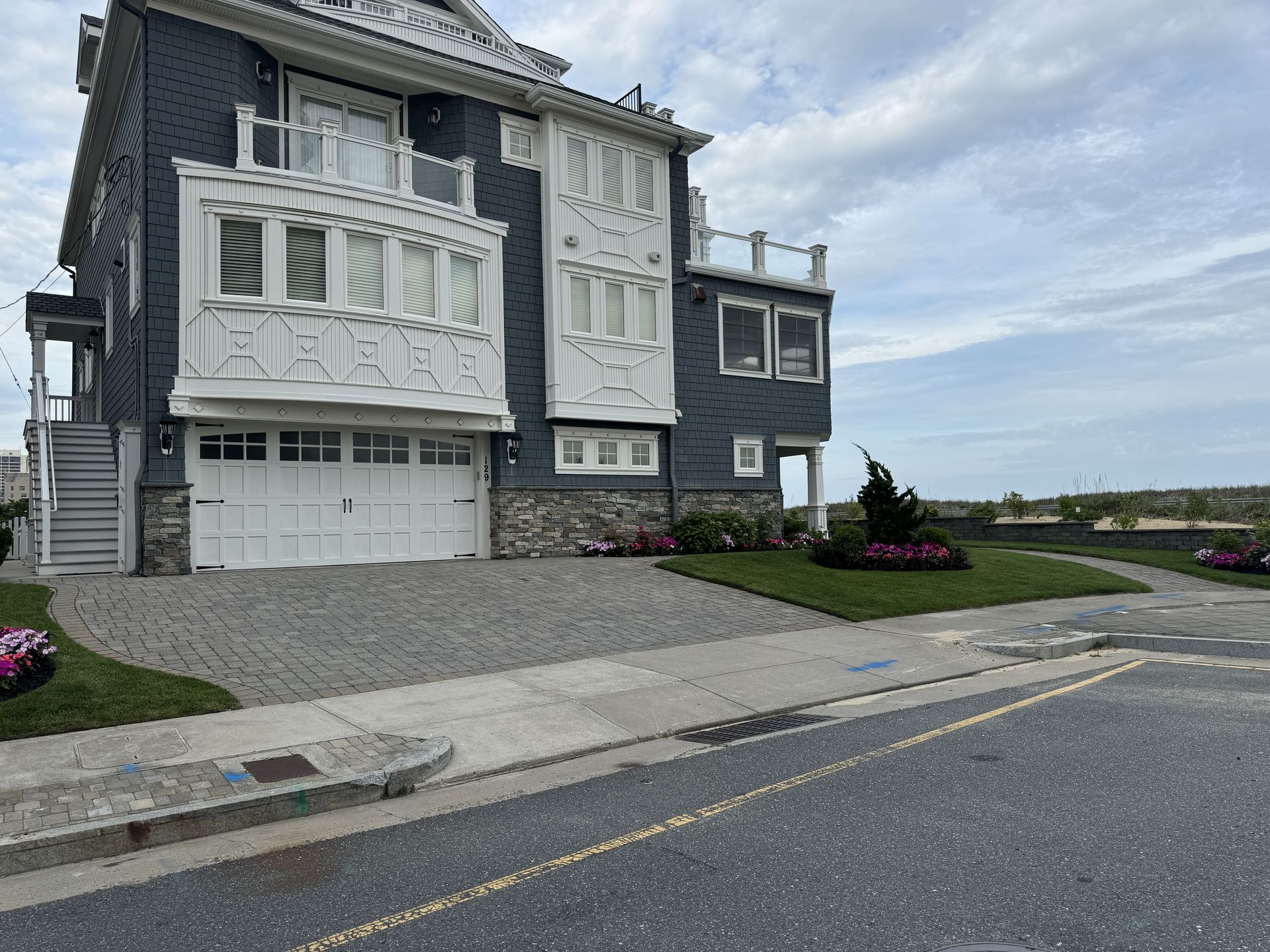 Coastal house with gray siding, white trim, garage, and a sloped driveway near the street