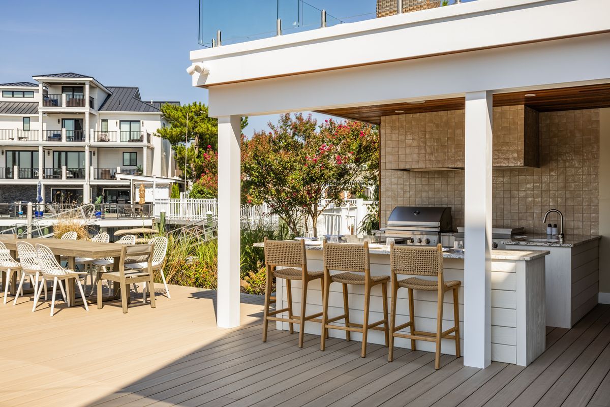 Outdoor patio with wooden tables and chairs beside a modern building and grill area