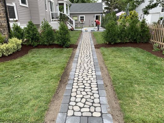 Stone walkway leading to a white house with landscaped lawns and shrubs