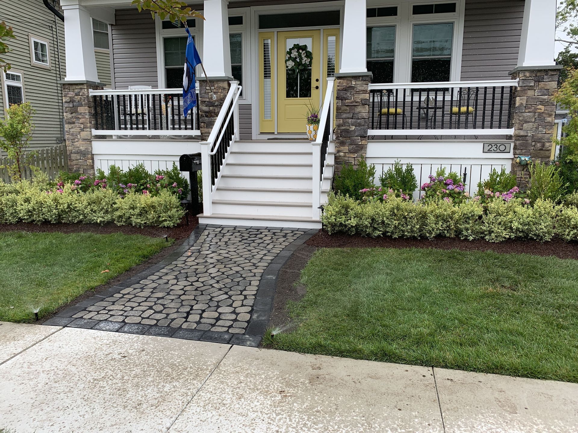 Front porch with white steps, yellow door, stone walkway, and manicured lawn in front of a house